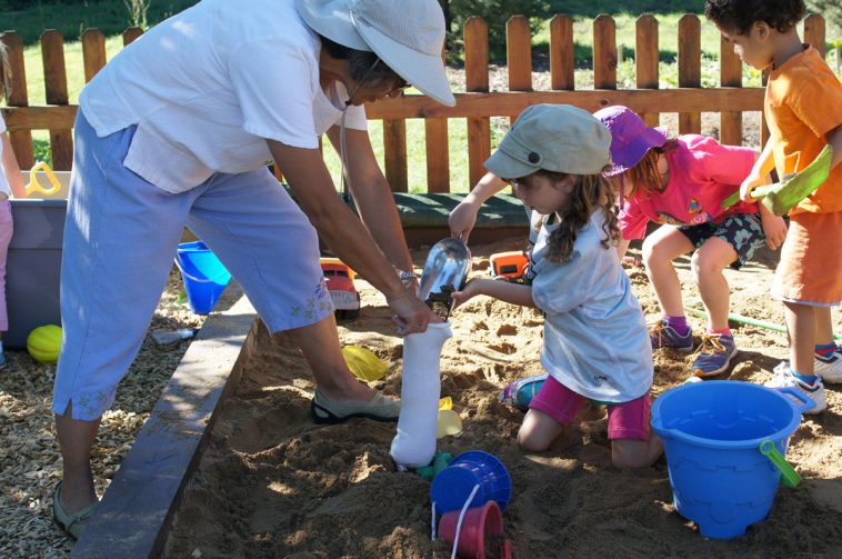 Kodo kids teacher helps a child in the sandbox