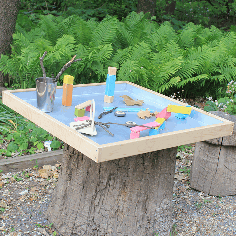 Maple wood activity tray with a reflective steel interior, set on a tree stump with colorful blocks and nature items.