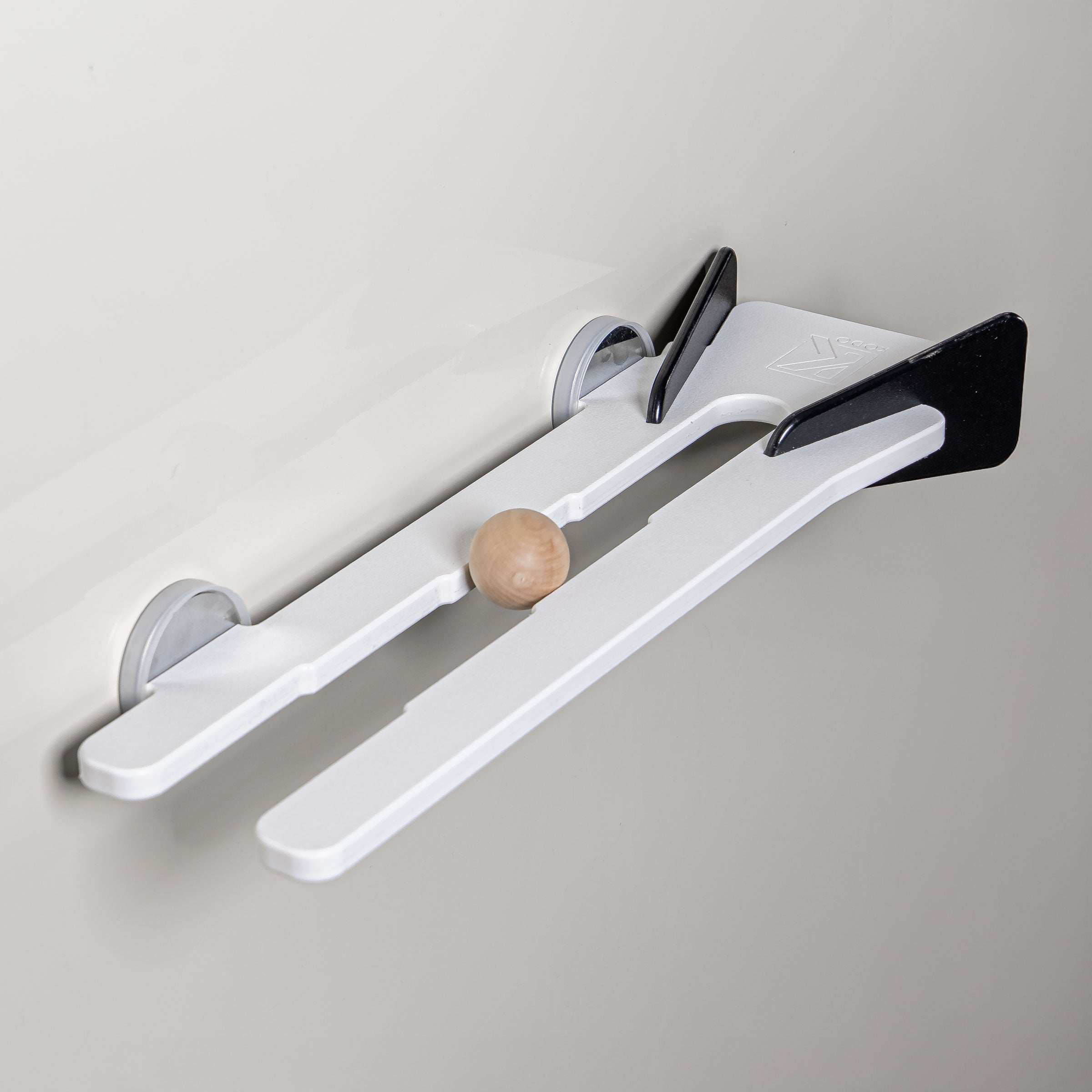 White wall-mounted shelf with black accents and a small wooden ball resting in the center track.