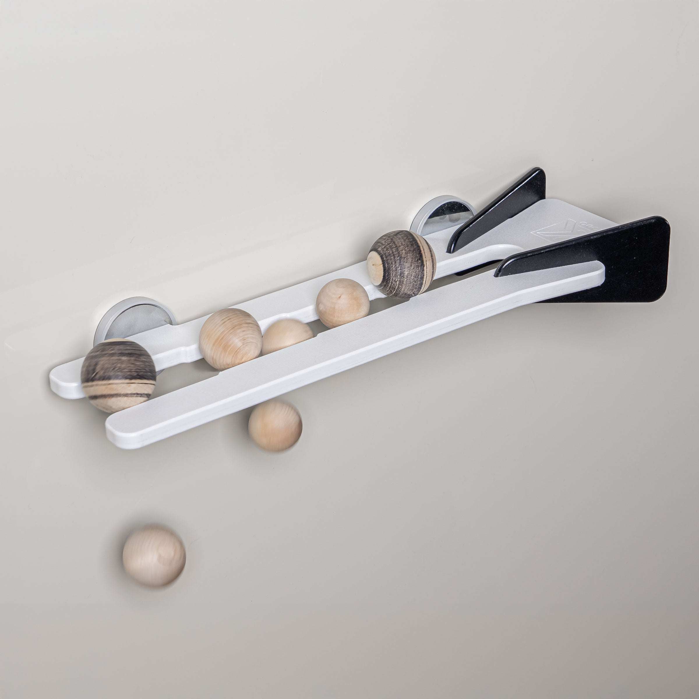 Wall-mounted white and black track toy with wooden spheres rolling down the parallel rails.