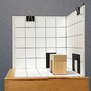 Wooden building blocks on a white grid base with black shadow silhouettes, set against a matching grid backdrop.