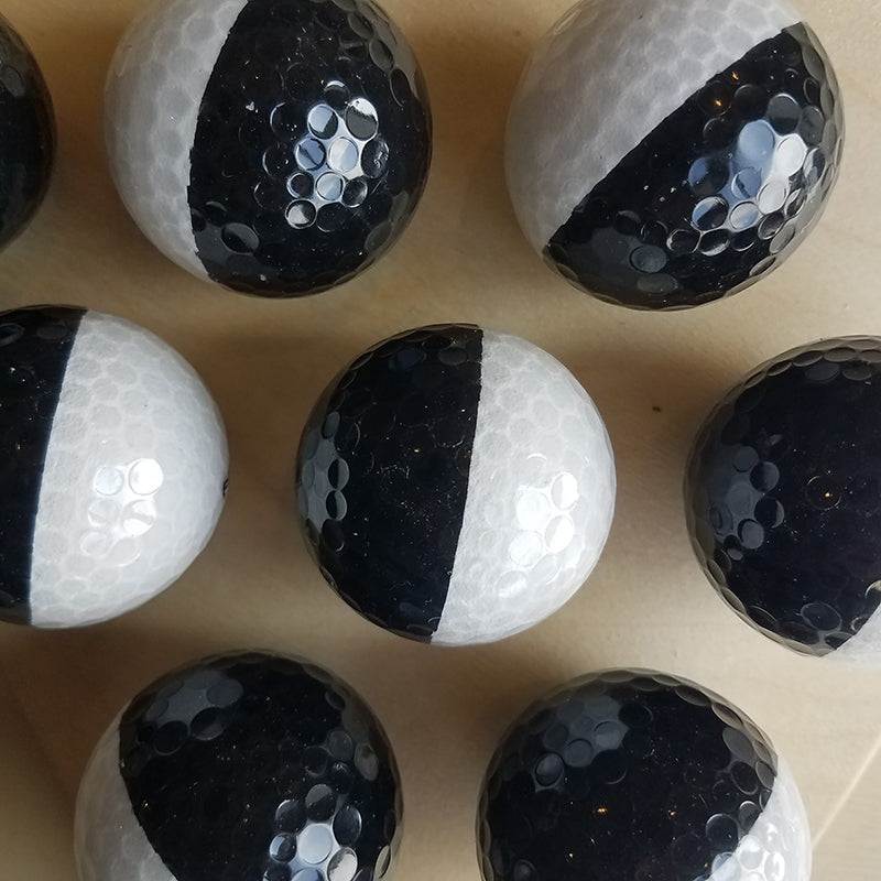 Textured black and white balls with a dimpled surface arranged on a flat wooden surface.