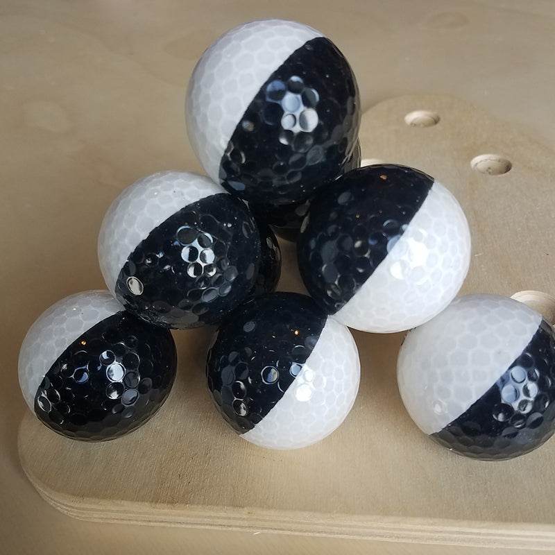 Textured black and white balls with a dimpled surface, stacked on a wooden base for sensory play and learning.