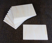 Set of ten smooth, rectangular light-colored wooden building boards arranged in a stack on a patterned surface.