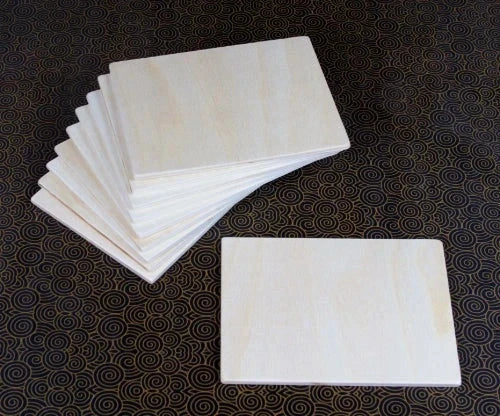 Set of ten smooth, rectangular light-colored wooden building boards arranged in a stack on a patterned surface.