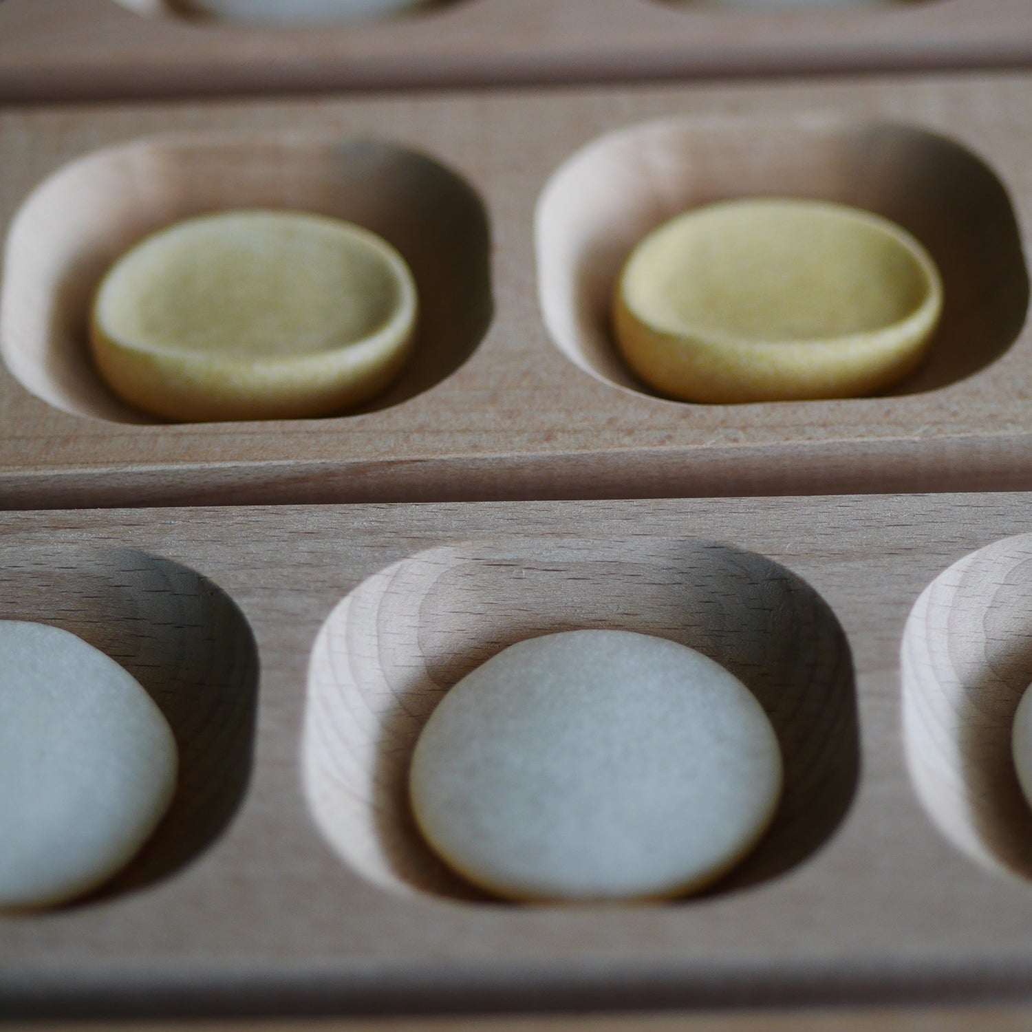 Smooth, round calming stones in various neutral colors nestled in a light wooden tray with carved circular compartments.