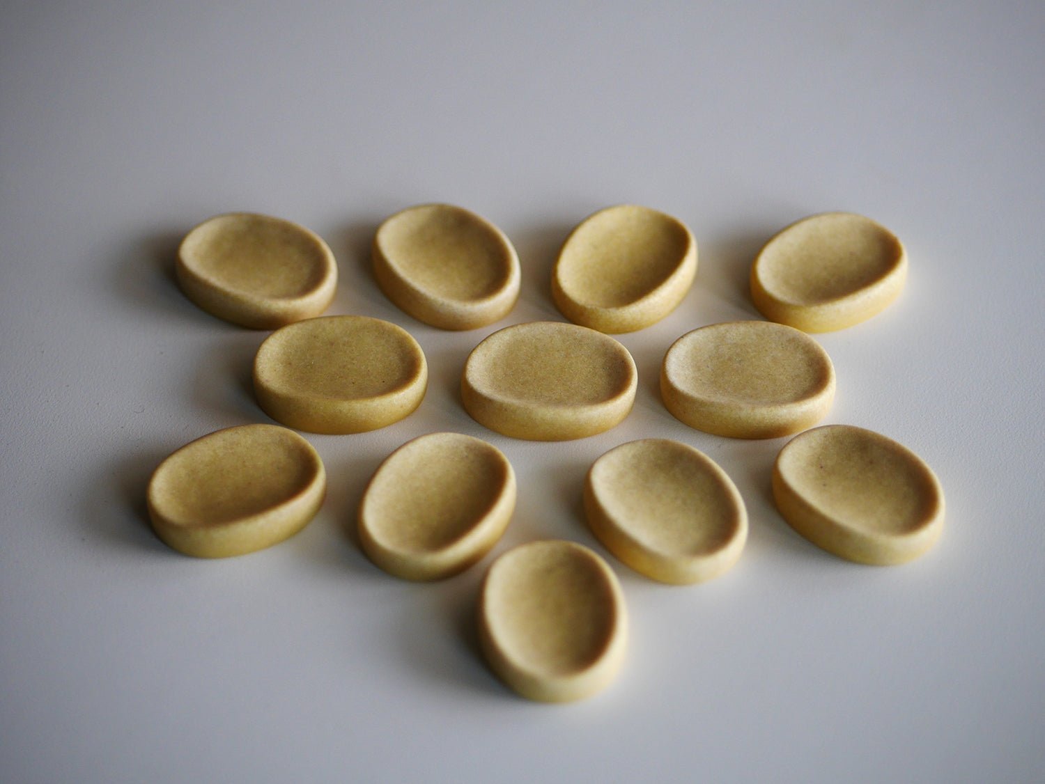 Set of ten smooth, tan, oval-shaped calming stones with concave centers arranged on a white surface.