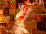 Uncle Goose basswood alphabet blocks with colorful letters and animal illustrations next to a branded canvas drawstring bag.