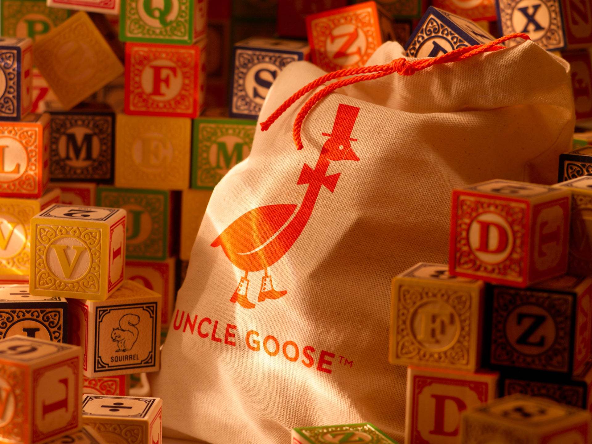 Uncle Goose basswood alphabet blocks with colorful letters and animal illustrations next to a branded canvas drawstring bag.