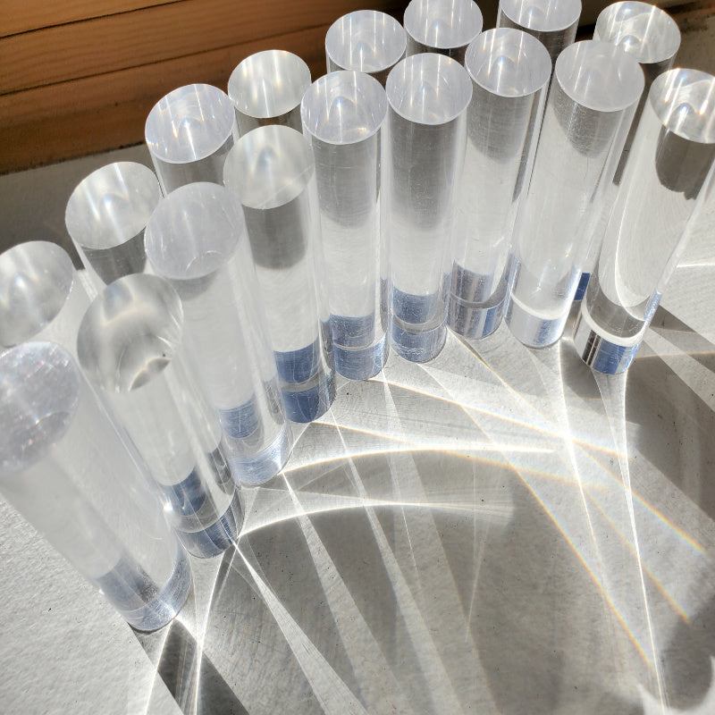 Set of 20 clear, cylindrical acrylic pegs casting light refractions on a white surface.
