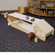 Kid-powered wooden conveyor belt toy with a hand crank, white fabric belt, and various wooden and felt play objects.