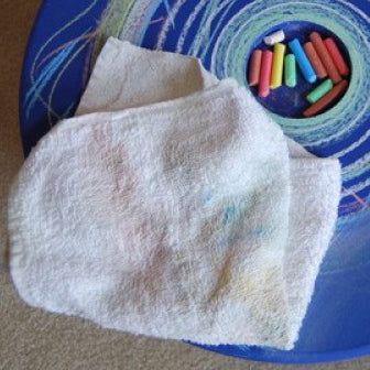 White cotton terry cloth towel resting on a blue Chalkspinner surface next to colorful chalk sticks.