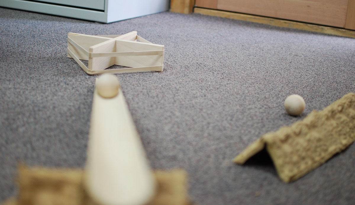 Natural wood deflector set pieces arranged on a gray carpet with wooden balls for geometry and ramp play.