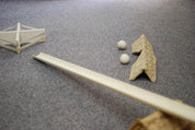 Wooden ramp, textured cardboard deflector, and two small wooden balls arranged on a grey carpet surface.