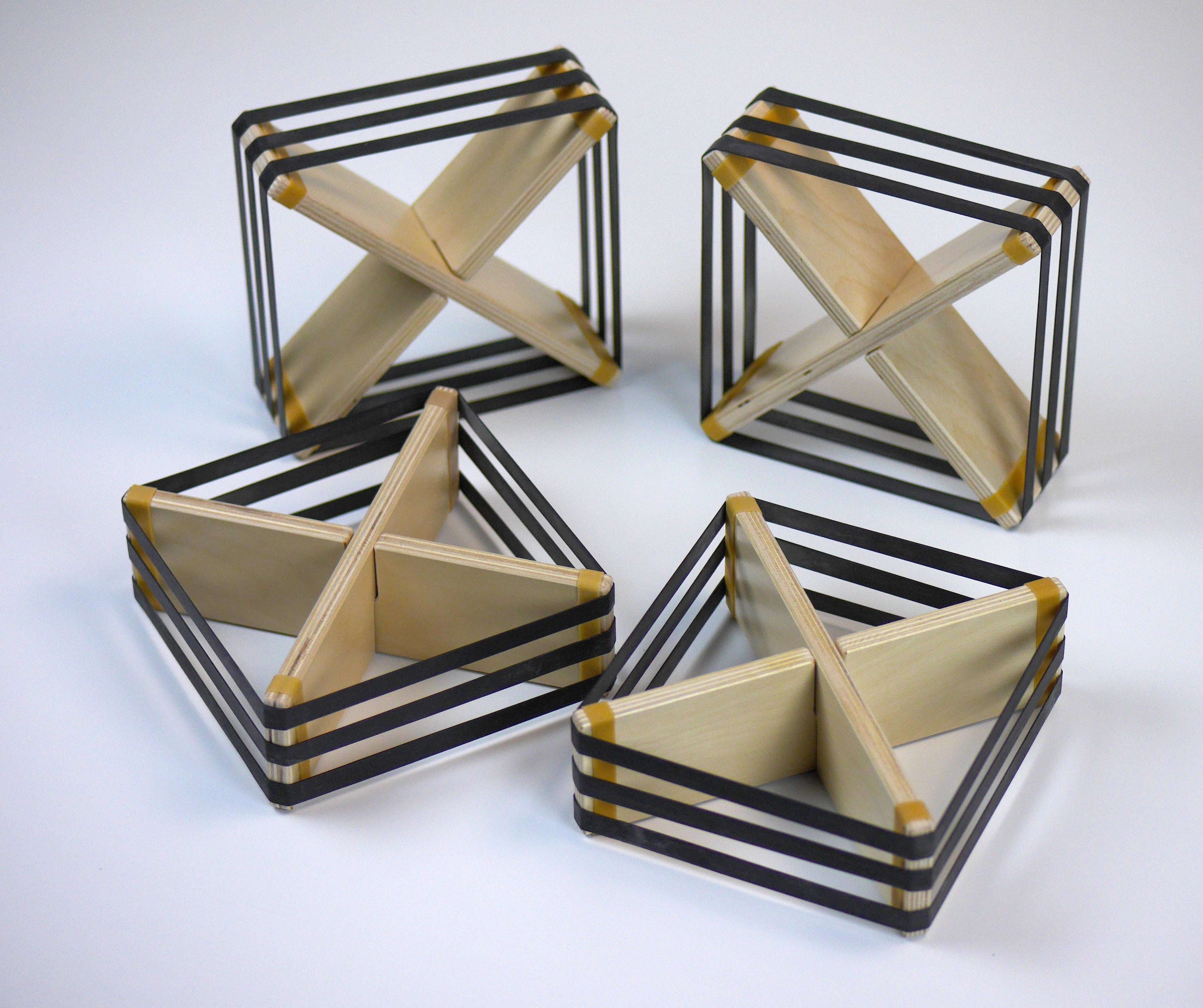 Four square wooden deflectors with cross-shaped centers and black elastic bands on a white background.