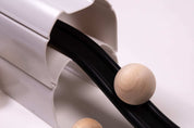 Natural wood spheres rolling down a black track supported by a white plastic ramp structure.