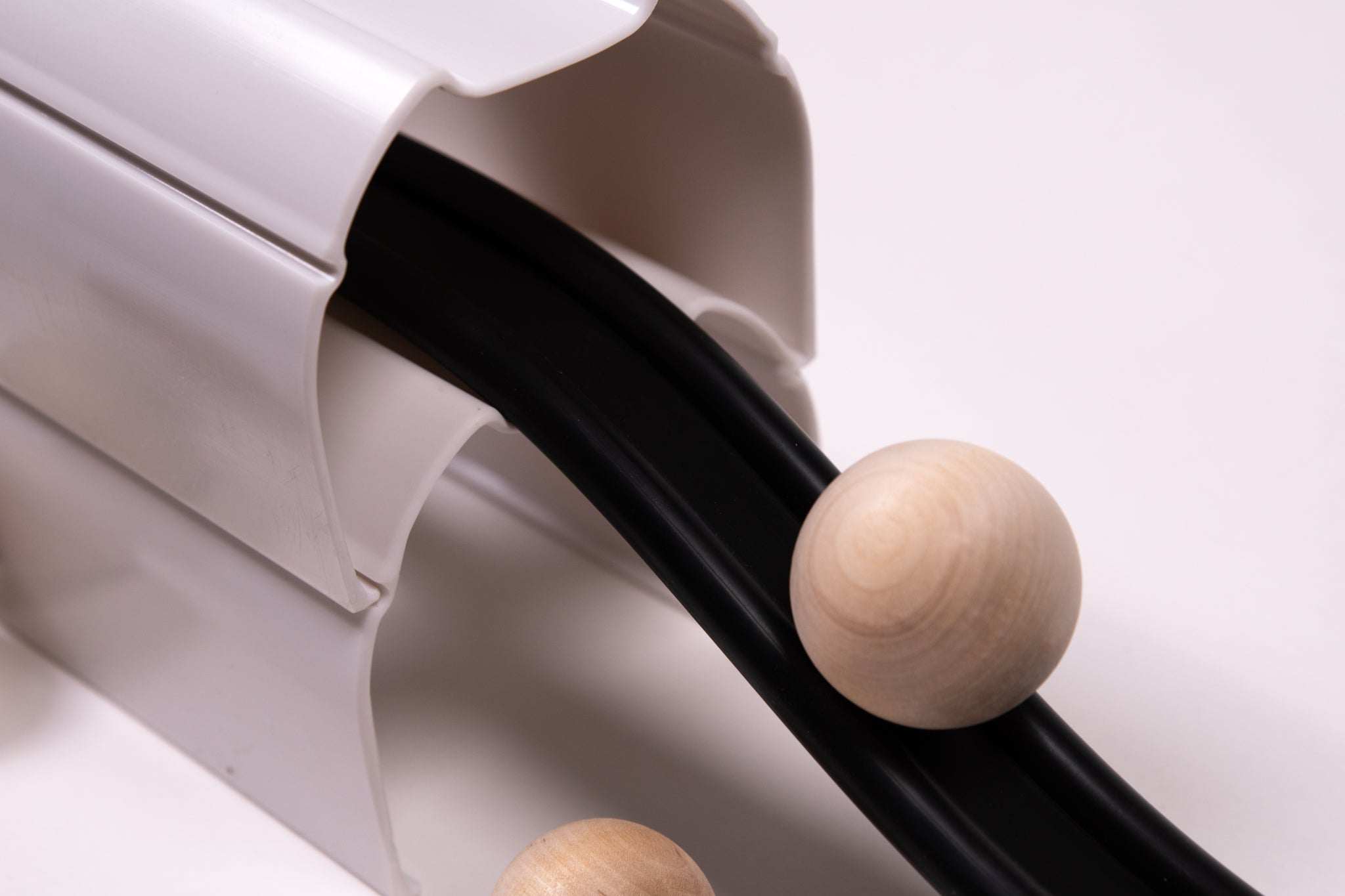 Natural wood spheres rolling down a black track supported by a white plastic ramp structure.