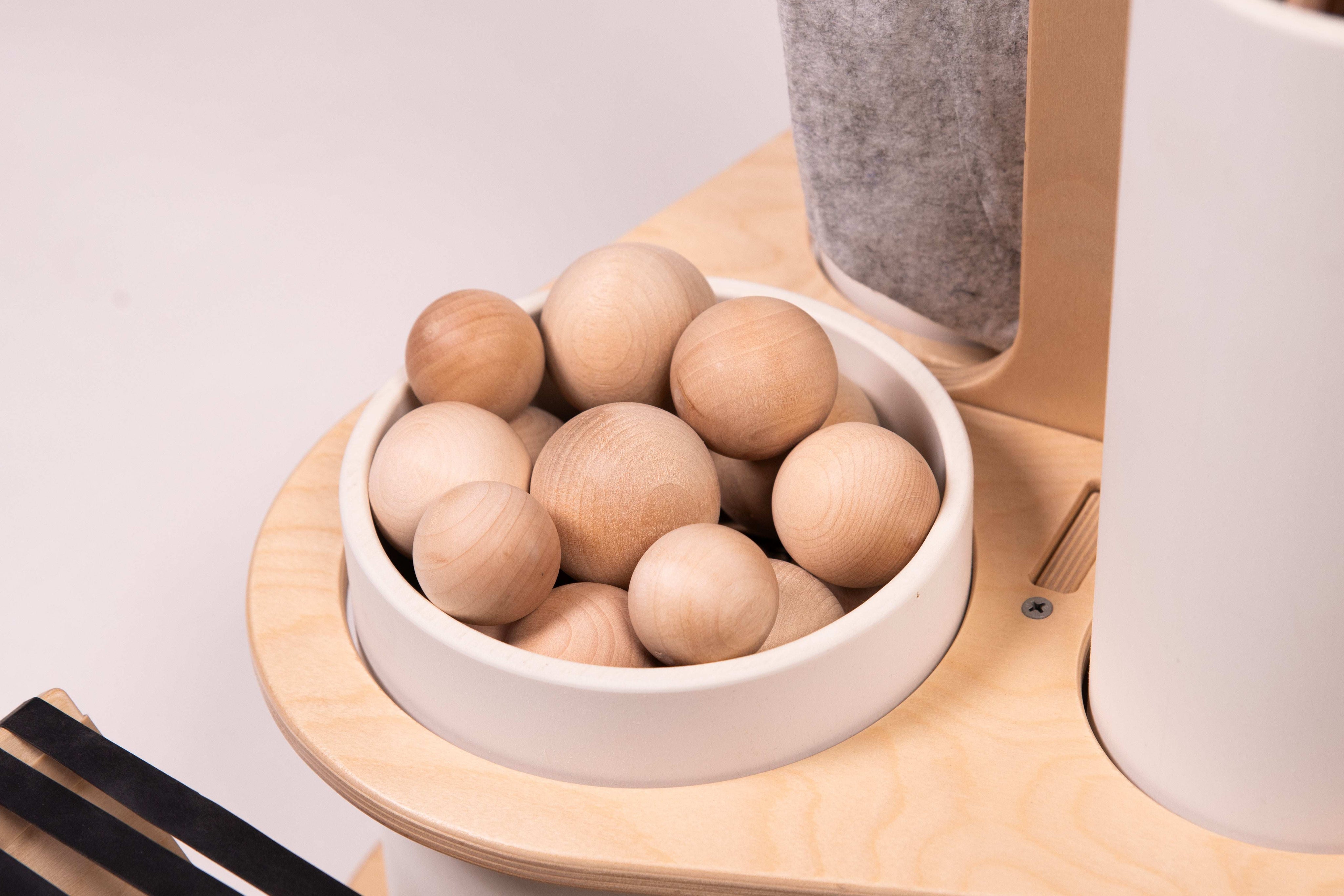 Natural wooden balls in a white ceramic bowl on a light birch wood caddy with a grey canvas storage pouch.
