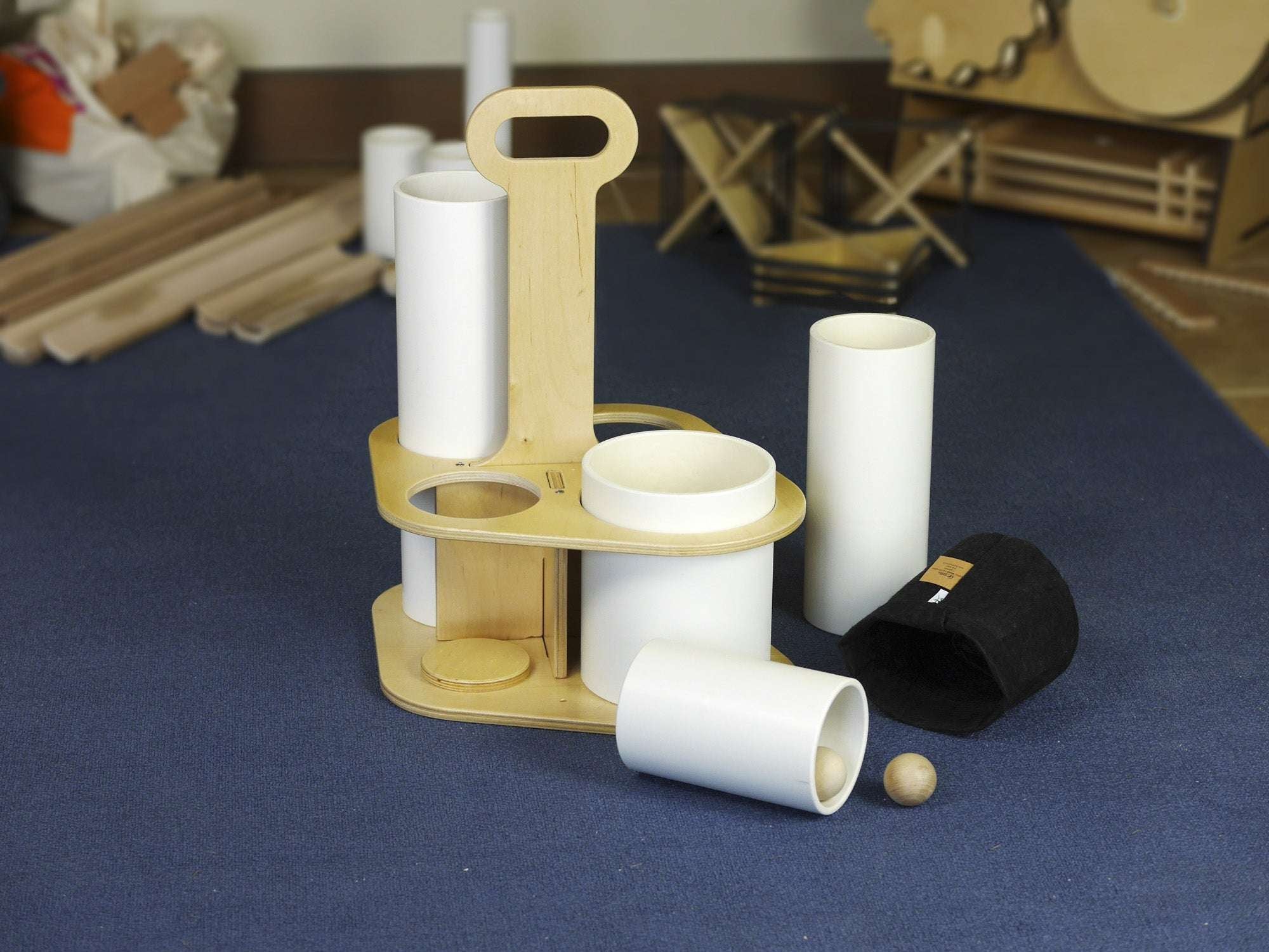 Wooden caddy with white tubes, a black canvas storage pouch, and a small wooden ball on a blue carpet.