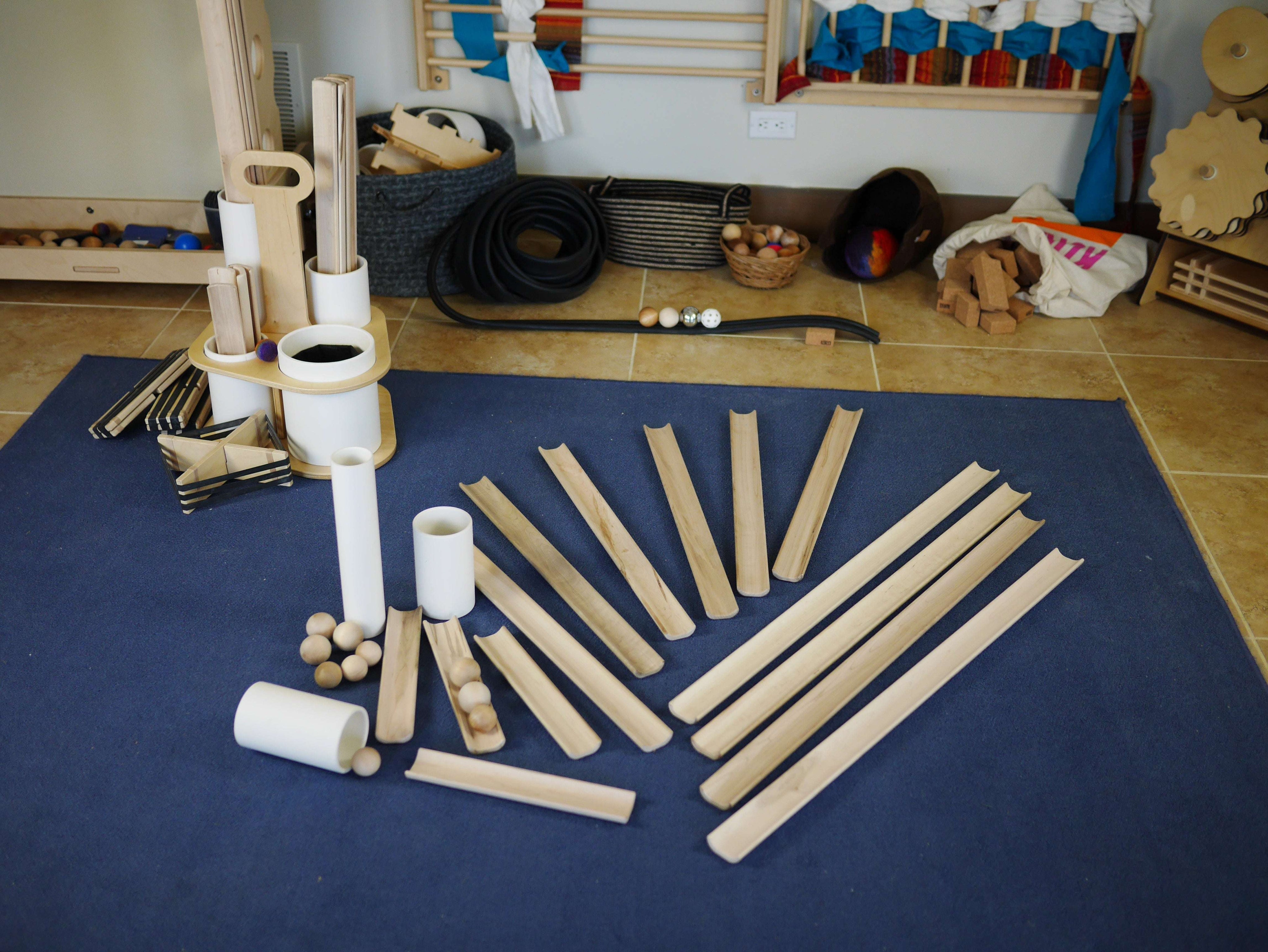 Hand-finished wooden ramps and white tubes with wooden balls arranged on a blue rug for STEM play.