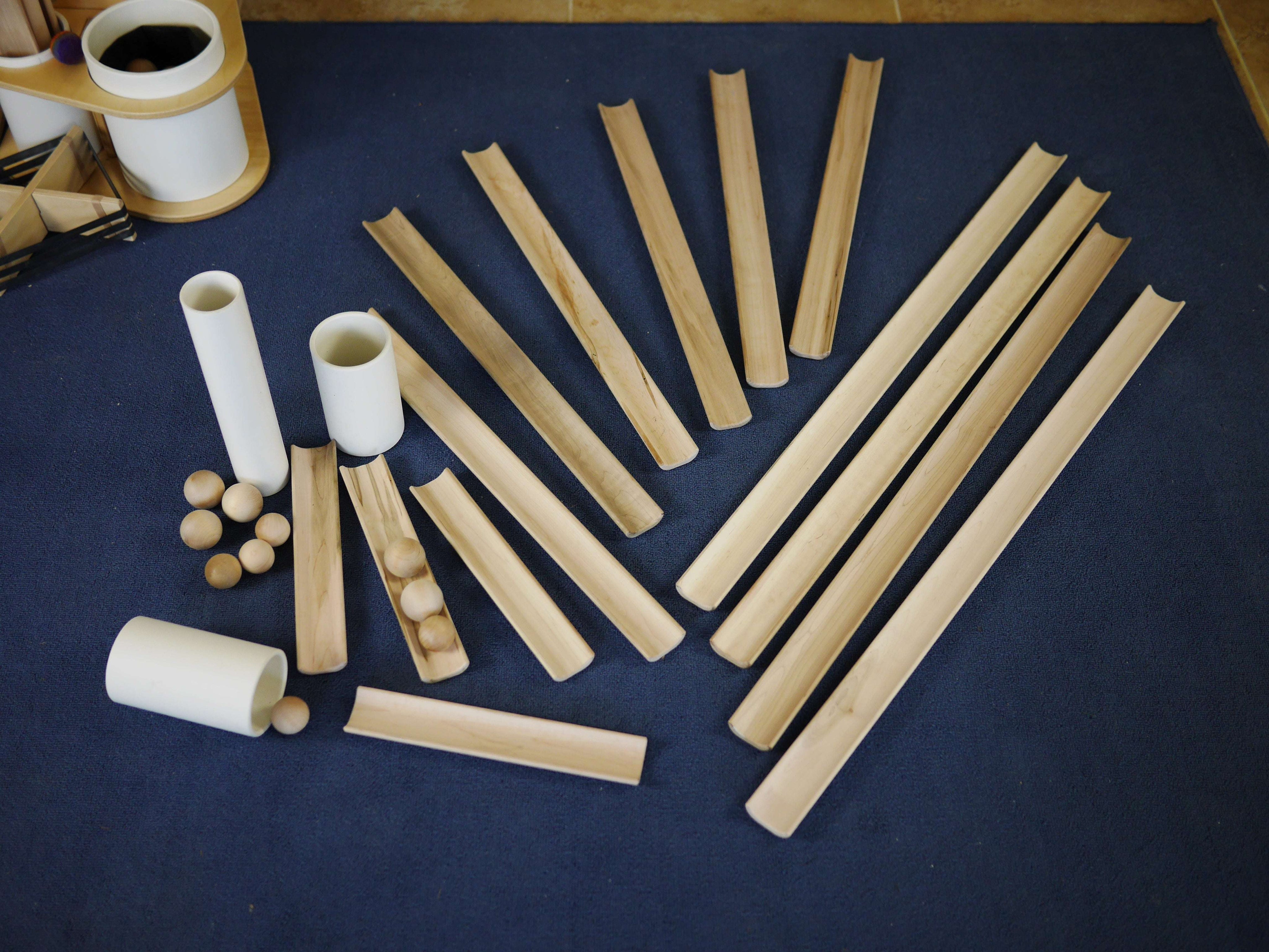 Hand-finished wooden ramps, white tubes, and small wooden balls for a STEM building set arranged on a blue mat.