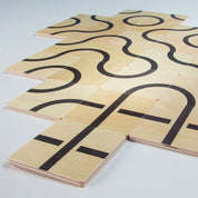 Square wooden tiles with black printed curves and lines arranged to create continuous patterns on a white surface.