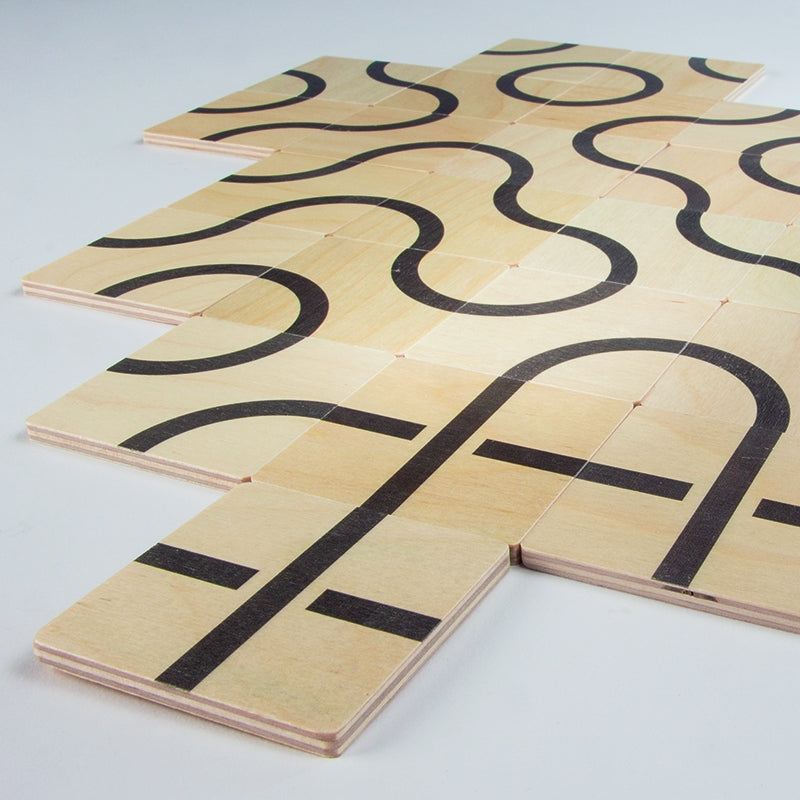 Square wooden tiles with black printed curves and lines arranged to create continuous patterns on a white surface.