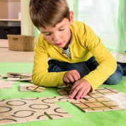 Child arranging square wooden tiles with black geometric patterns on a green mat.