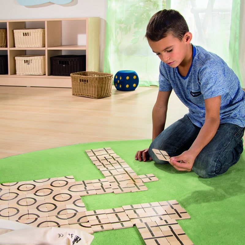 Boy kneeling on a green rug arranging square wooden tiles with black geometric patterns into creative designs.