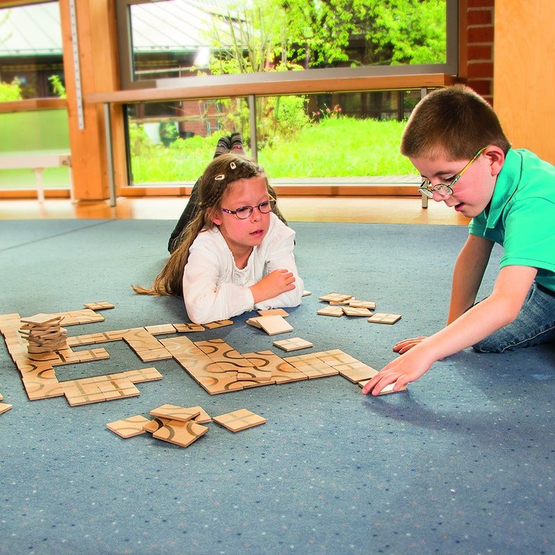 Children playing with wooden square tiles featuring black curved patterns on a blue carpet.