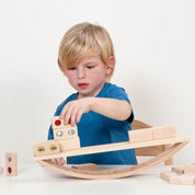 Child playing with a wooden experimental seesaw, stacking beech blocks with colorful inserts to learn about balance.