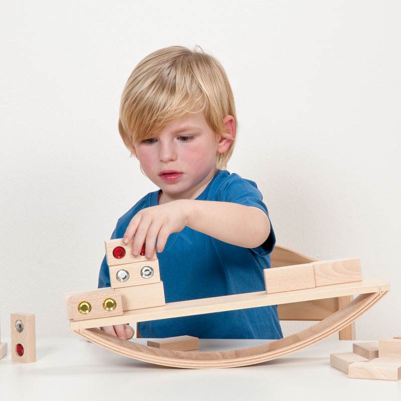 Child playing with a wooden experimental seesaw, stacking beech blocks with colorful inserts to learn about balance.