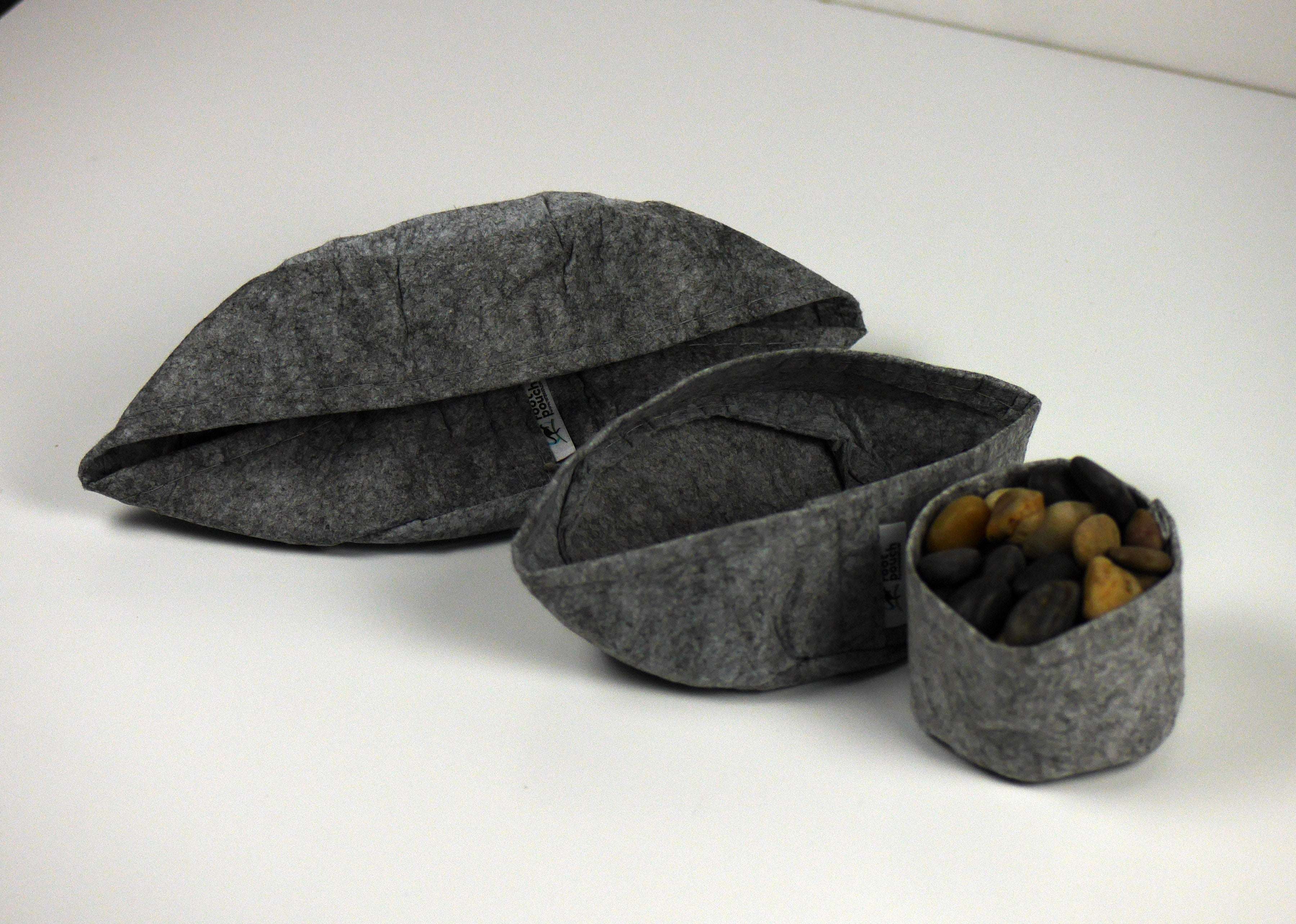 Three grey felt fabric bowls of varying sizes, with the smallest filled with smooth river stones.