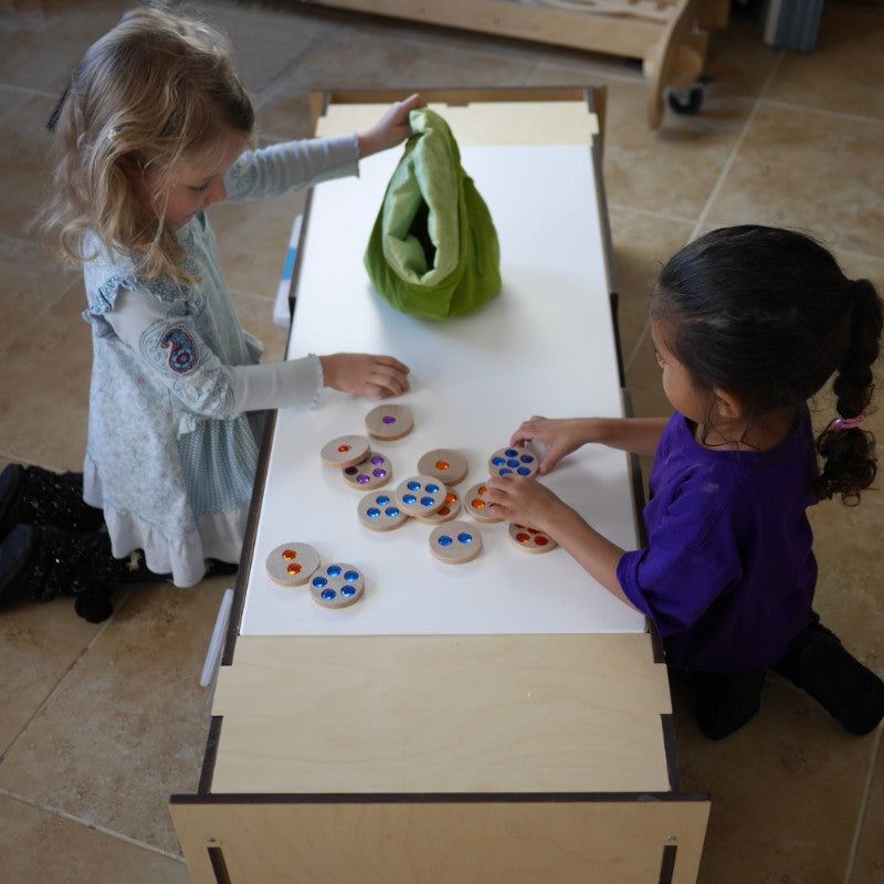 Two children playing with 36 wooden discs inlaid with colorful, sparkly gems on a white table.