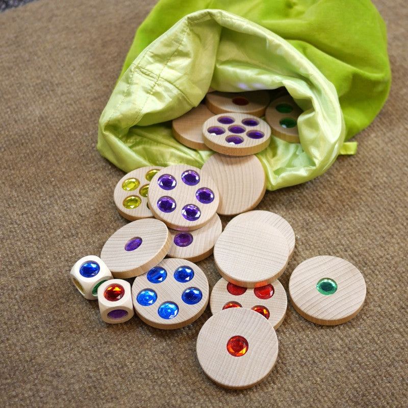 Wooden discs with colorful embedded gems spilling from a green velvet drawstring bag on a textured surface.