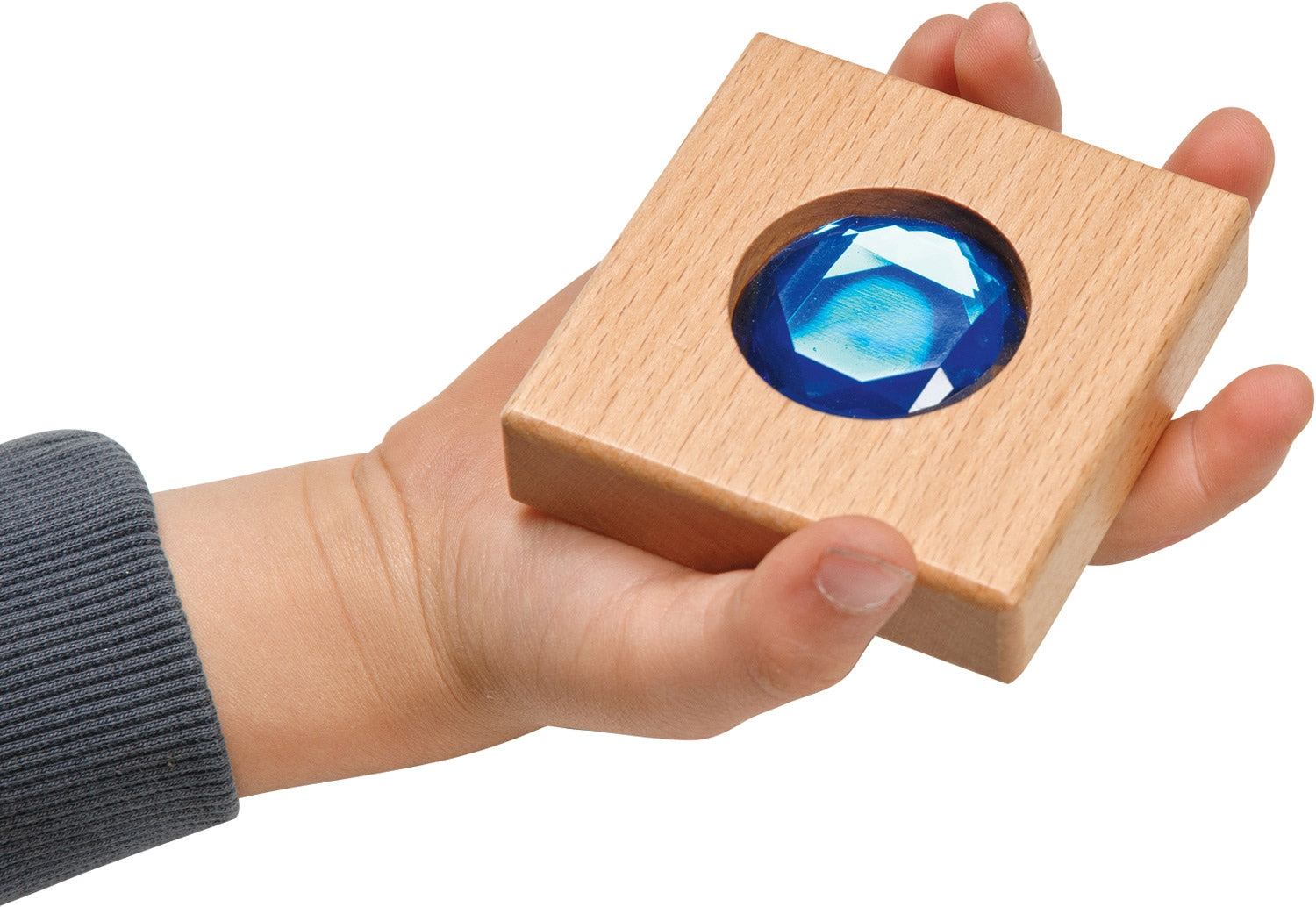 Child holding a chunky square wooden tile featuring a large, faceted blue gemstone insert.