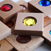 Chunky wooden square tiles featuring vibrant, oversized faceted gemstones in red, blue, and yellow for sensory play.