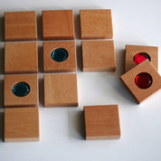 Chunky wooden square tiles with inlaid vibrant red and blue gemstones for sensory matching and cognitive play.