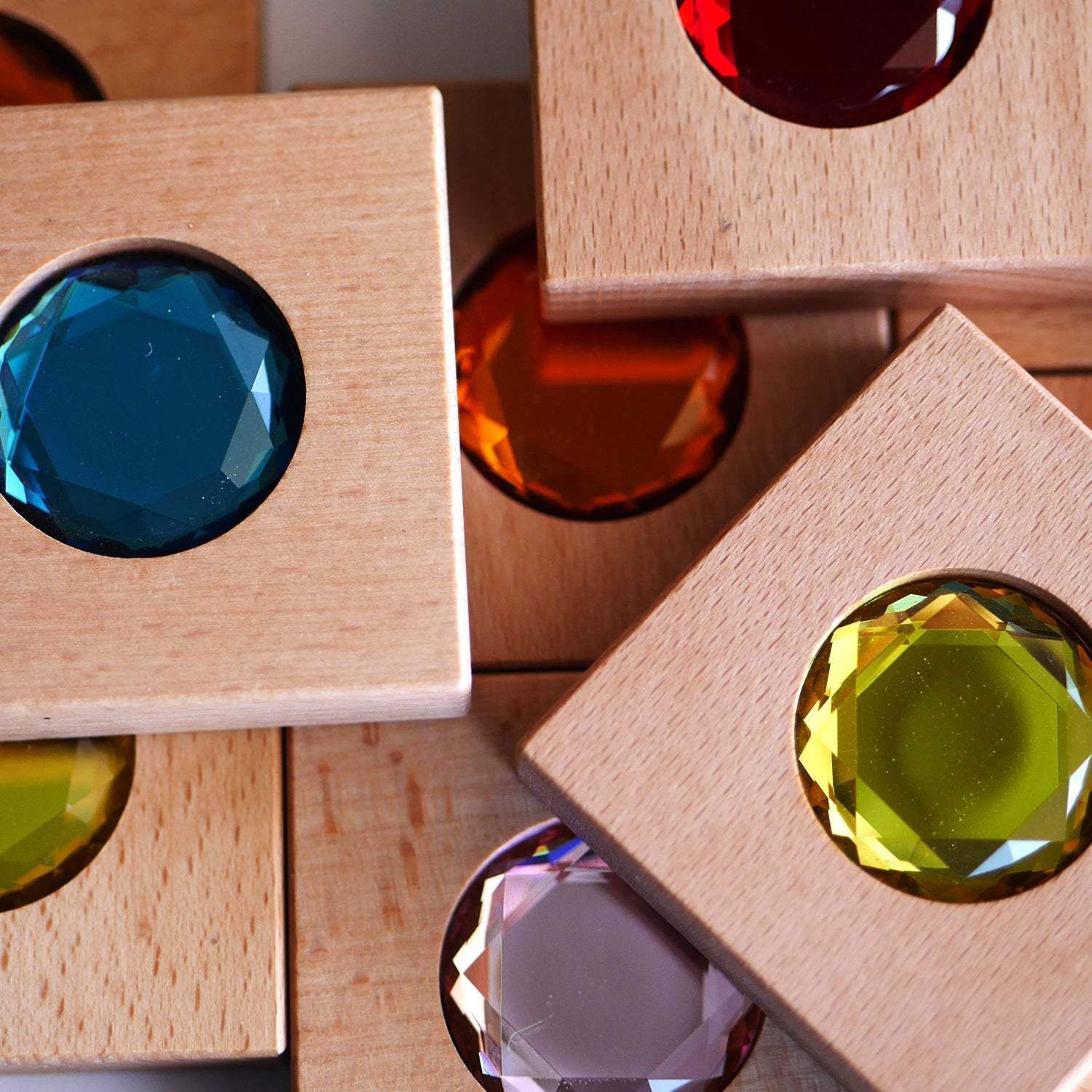 Chunky wooden square tiles featuring vibrant, faceted, multicolored gemstones for sensory play and color matching.