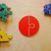 Wooden geometric puzzle set with a red circular piece and colorful jigsaw shapes on a light wood surface.
