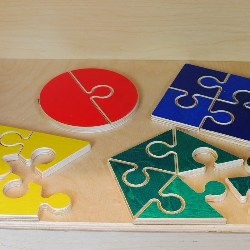 Wooden geometric jigsaw puzzles in red, blue, yellow, and green on a light wood surface for kids' spatial learning.
