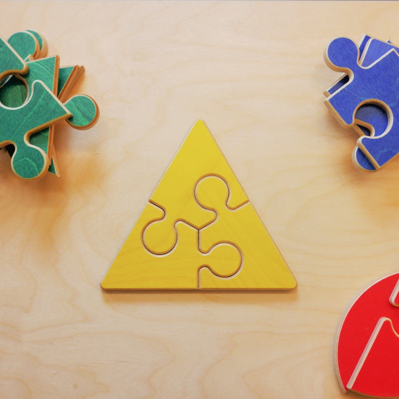 Wooden geometric puzzle set with yellow triangle pieces and colorful jigsaw shapes on a light wood surface.