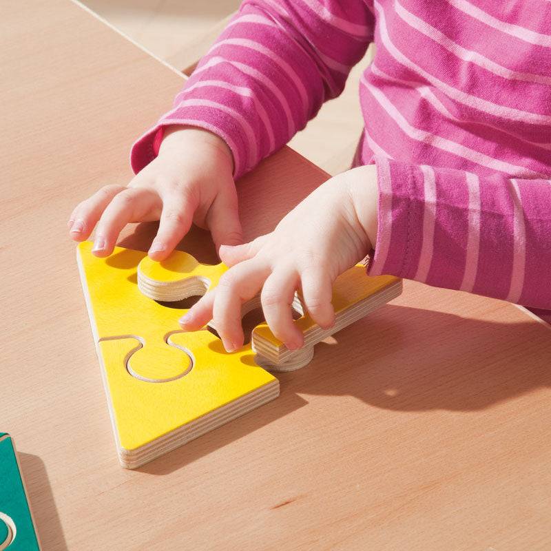 Child playing with a yellow wooden geometric jigsaw puzzle piece on a table.