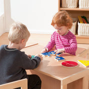 Two children playing with colorful wooden geometric jigsaw puzzles on a small wooden table.