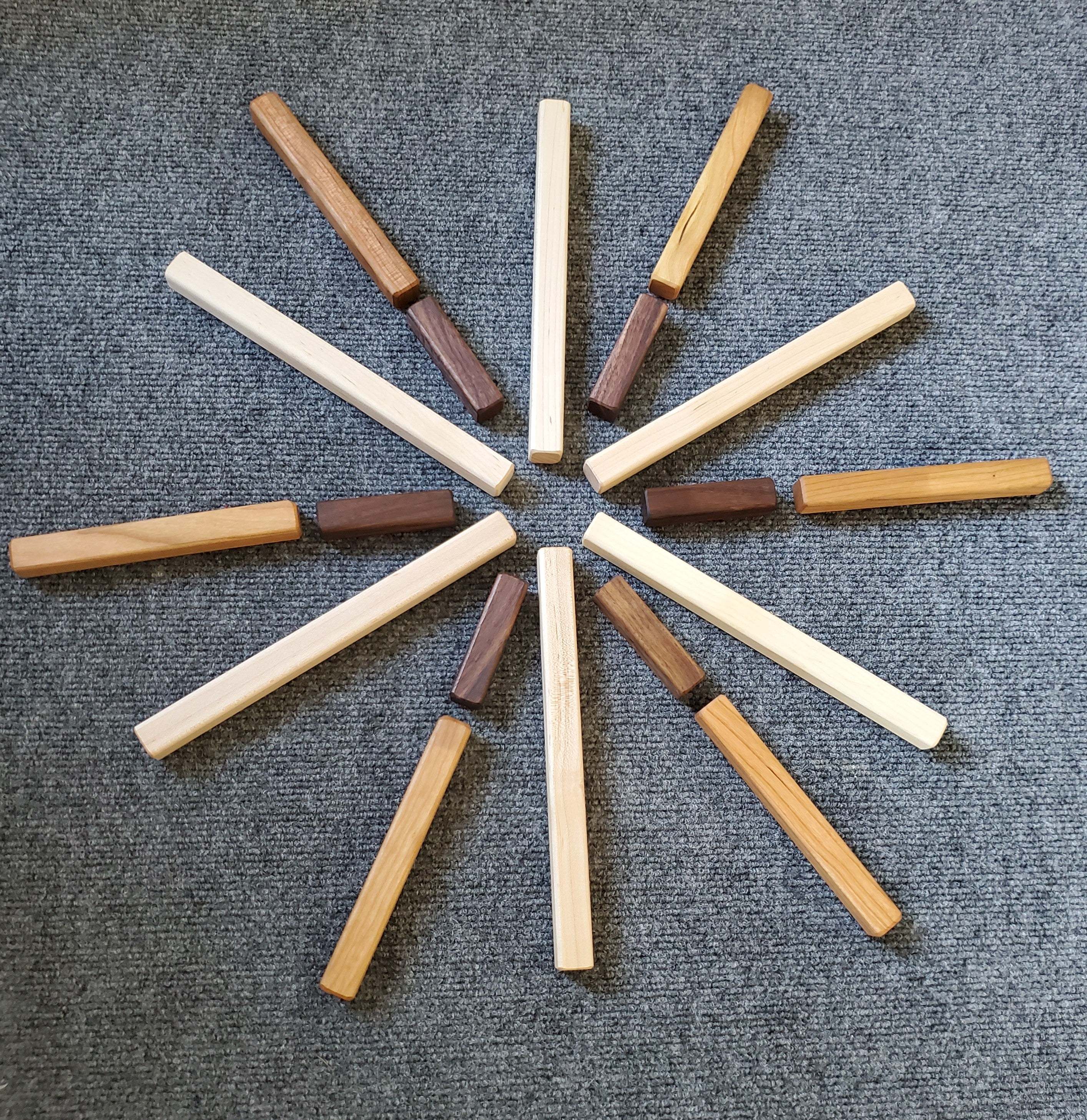 Set of graduated wooden building sticks in various natural wood tones arranged in a circular star pattern.