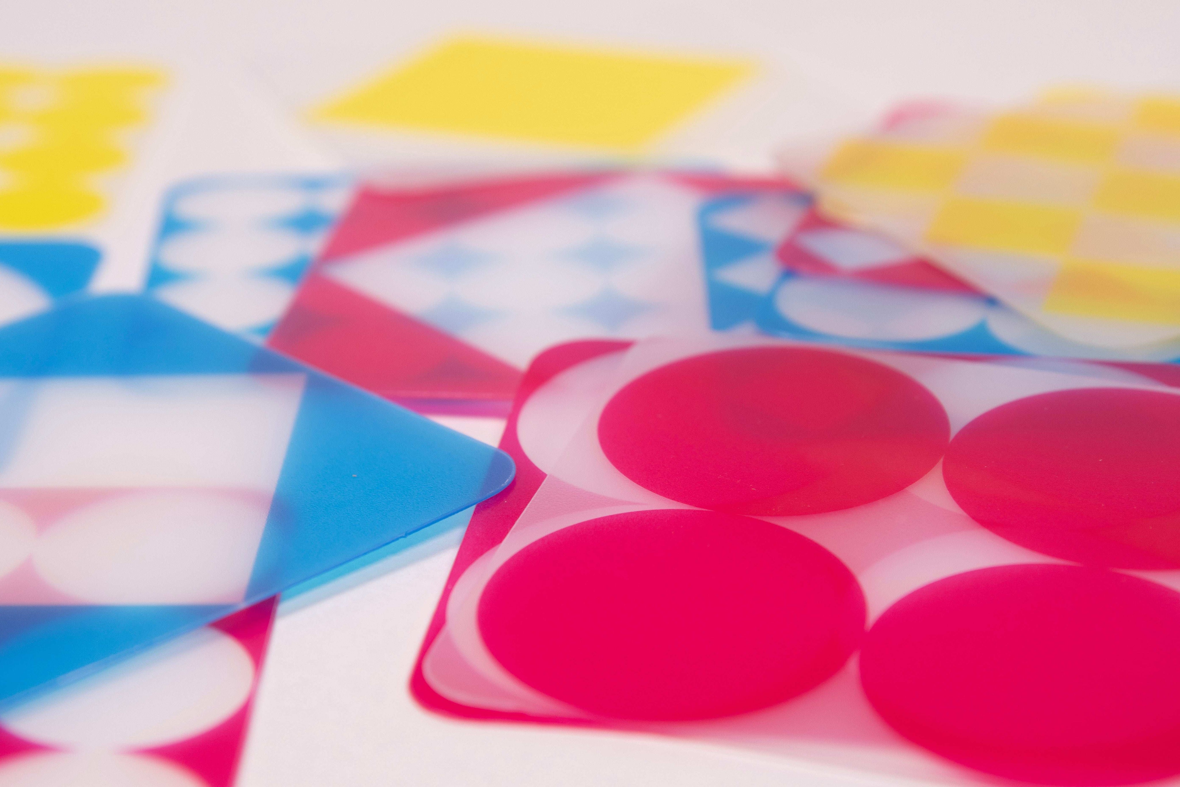 Transparent red, blue, and yellow geometric cards with circles and squares for STEM learning and color mixing.