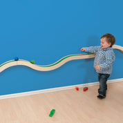 Toddler playing with a wooden Hill and Valley wall-mounted track featuring green paths and rolling balls on a blue wall.