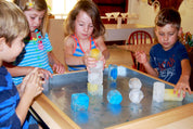 Children stacking colorful, geometric ice cubes on a metal sensory tray for creative play.