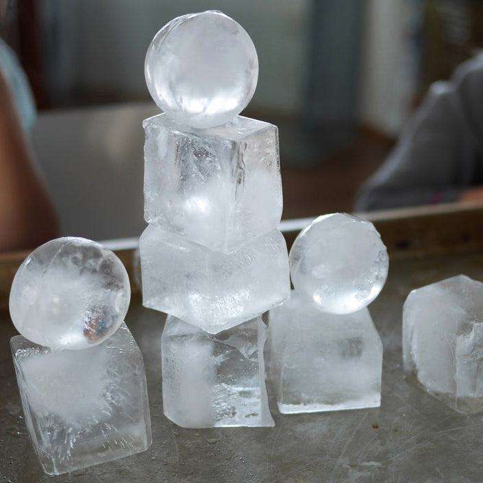 Clear ice spheres and cubes stacked on a tray, demonstrating creative sensory and construction play with frozen shapes.