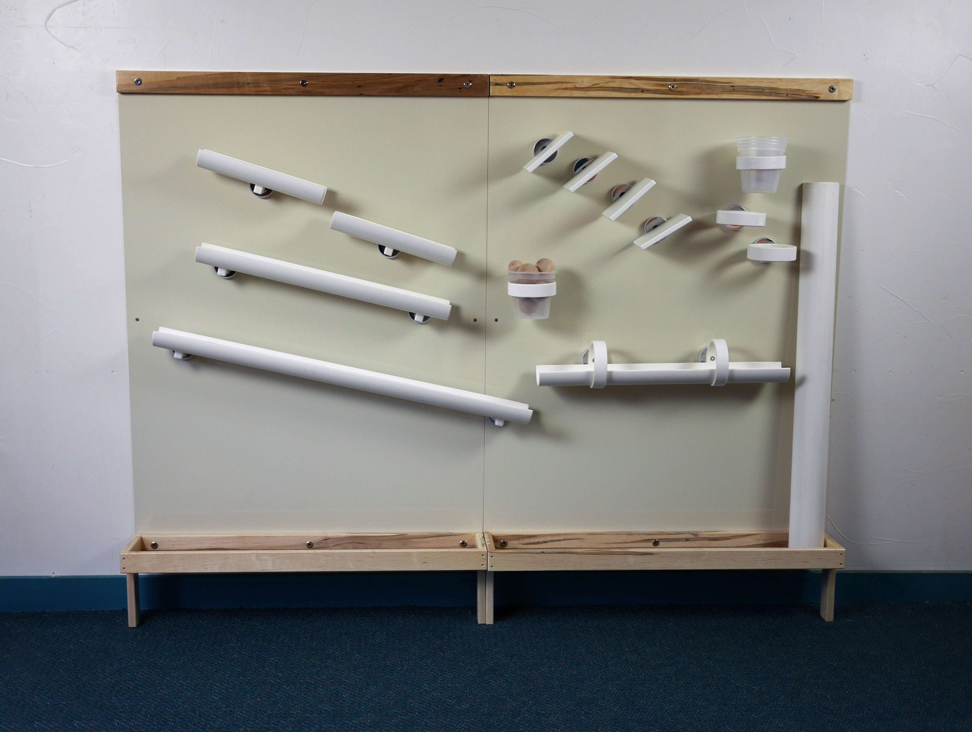 Two beige magnetic wall panels with Wormy Maple trim, featuring white magnetic ramps, cups, and balls for STEM play.